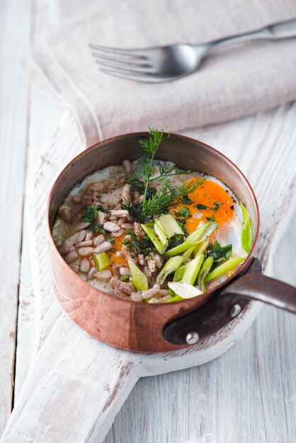 Scrambled eggs with greens in the copper pot on the white wooden table