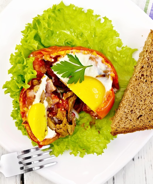 Scrambled eggs with ham and mushrooms in a tomato on a green lettuce in the plate bread fork on the background of the wooden planks on top