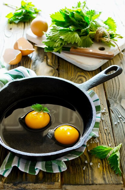 Scrambled eggs with nettles in a pan on a wooden table