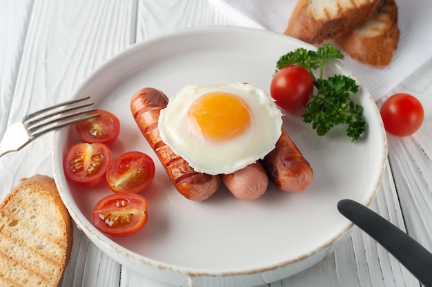 Uova strapazzate con salsicce, pomodori e toast su fondo di legno bianco