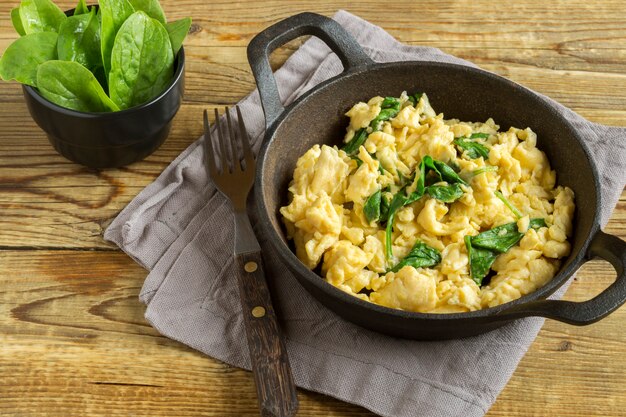 Scrambled eggs with spinach in a cast-iron pan. on a wooden table