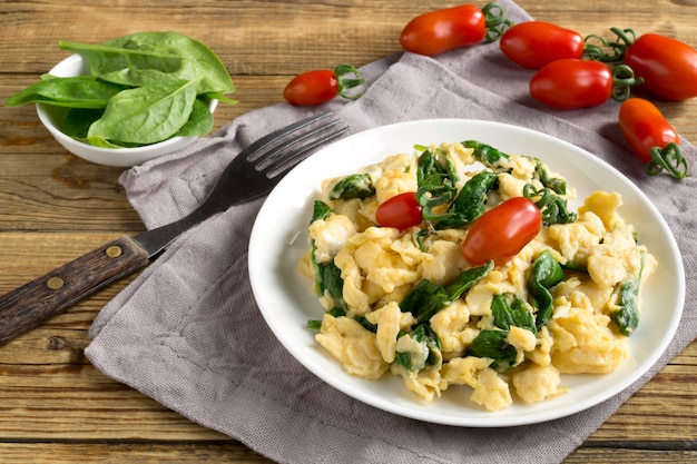 Scrambled eggs with spinach and tomatoes on a white plate. on a wooden table