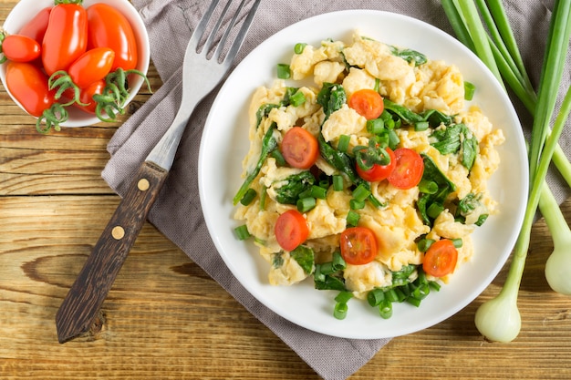 Scrambled eggs with spinach and tomatoes on a white plate. on a wooden table