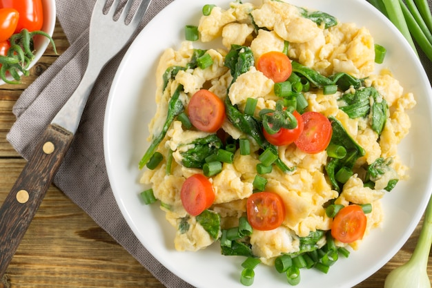 Scrambled eggs with spinach and tomatoes on a white plate.