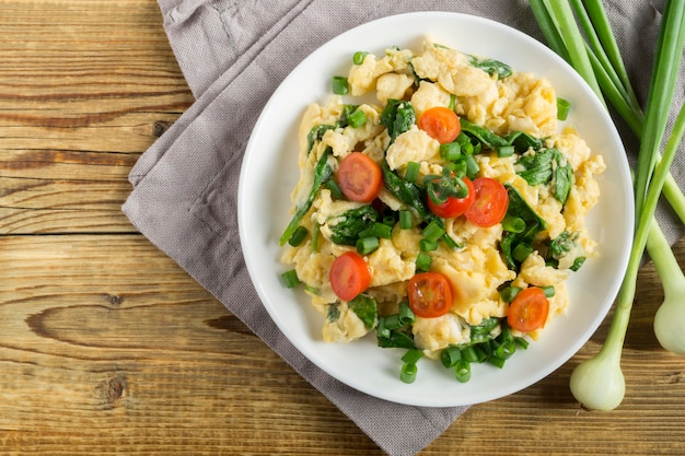 Scrambled eggs with spinach and tomatoes on a white plate.