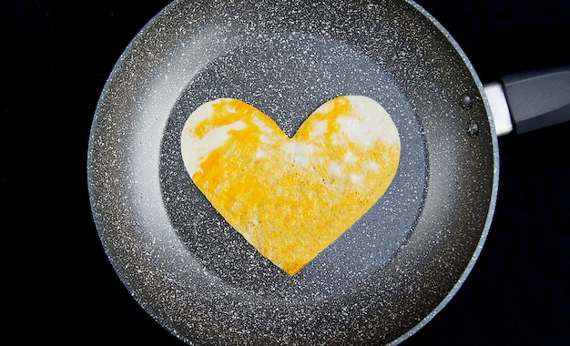 Фото Яичница в форме сердца на серой сковороде и черном фоне