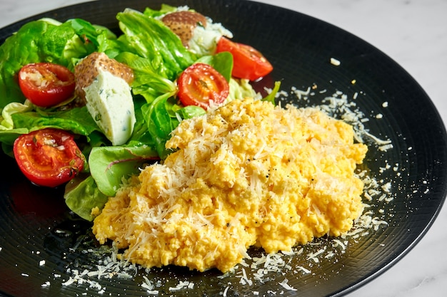 Scrambled omelet with spinach salad, ricotta cheese and cherry tomatoes, served in a black plate on marble