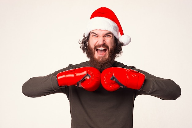 Screaming bearded man is holding hands together in boxing gloves.