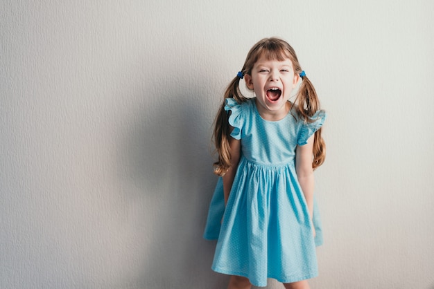 Screaming little girl in blue dress on neutral wall