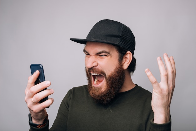 Screaming man is looking to his phone on white background.