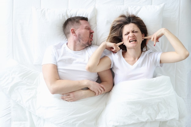 Screaming man lies in bed with depressed woman family problems and misunderstanding of each