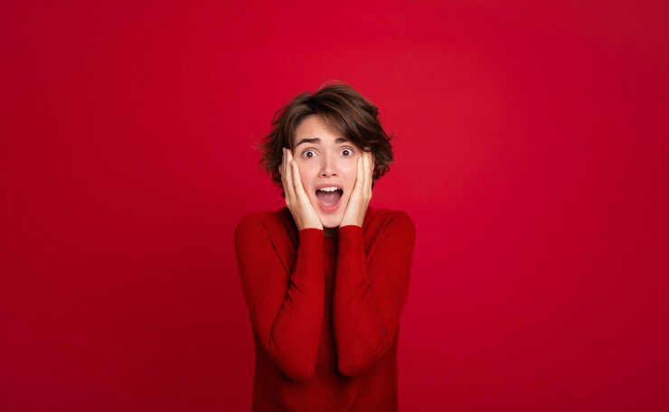 Photo 悲鳴をあげて 恐怖を感じる若い女性が 赤い鮮やかな背景に 顔を隠しながら を握っています