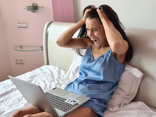 Screaming woman in bed in front of laptop monitor with bank card