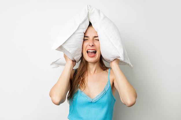 Кричащая молодая женщина закрывает уши подушкой на белом фоне