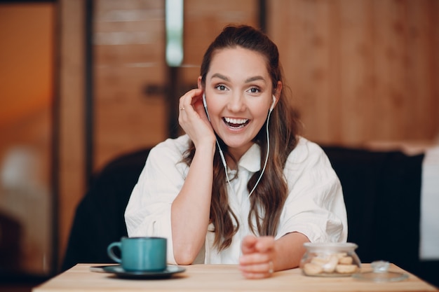 Экран приложения: улыбающаяся молодая женщина сидит за столом с ноутбуком и разговаривает по видеосвязи с другом или коллегой, счастливая девушка с чашкой чая или кофе выступает онлайн на веб-камеру конференции в помещении