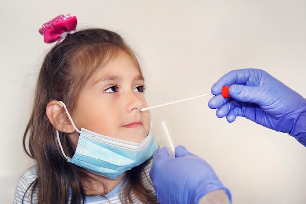 Screening virus, doctor taking nasal mucus test sample from nose performing respiratory virus testing procedure. Checking nasal cavity in ENT. girl in a protective face mask at doctor's appointment.