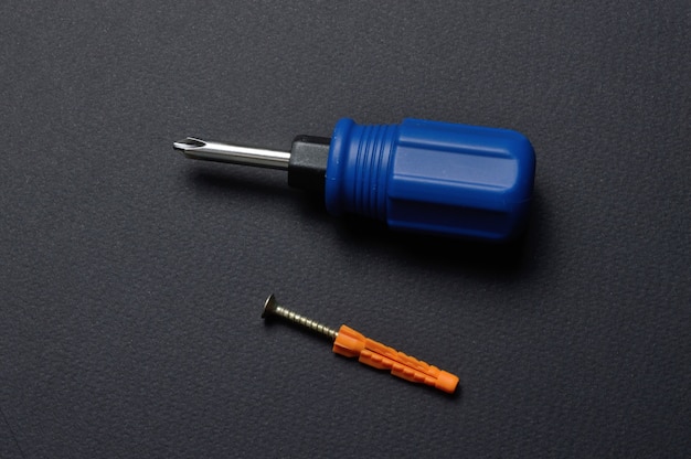 a screwdriver and a self-tapping screw with a dowel lie on a dark background close-up.