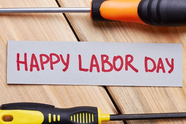 Screwdrivers and Labour Day card. Greeting paper on wooden plank. Festival for the workers.