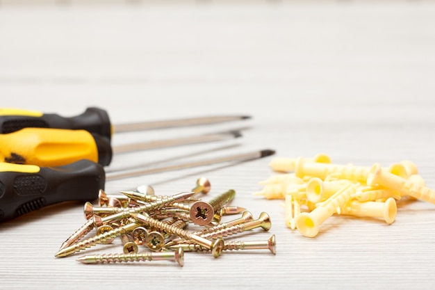 Screwdrivers and screws with plastic dowels on white wooden background