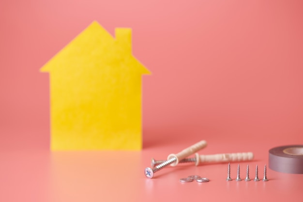 Screws and yellow house shaped figure on pink surface