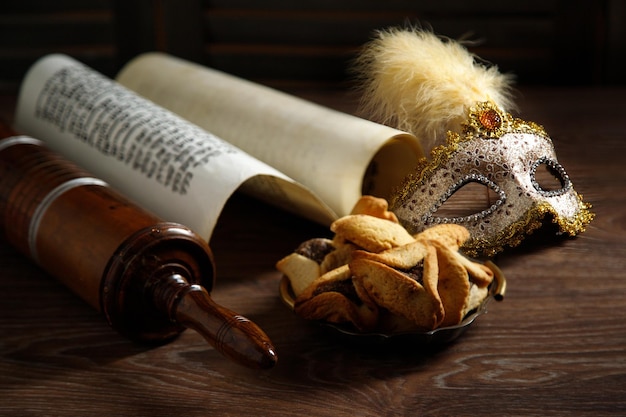 The Scroll of Esther and Purim Festival objects rattles masquerade mask Hamantaschen on a dark wooden table Rustic