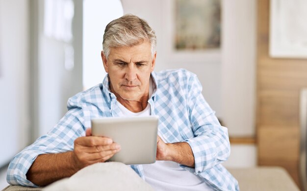 scrolling through websites shot of a mature man using his digital tablet while relaxing on his sofa at home