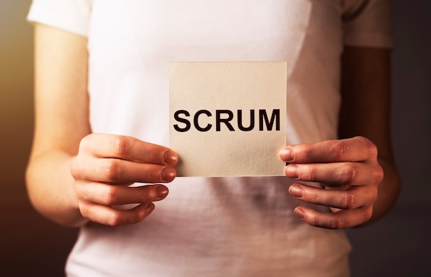 Scrum word on paper in female hand closeup concept of methods in management