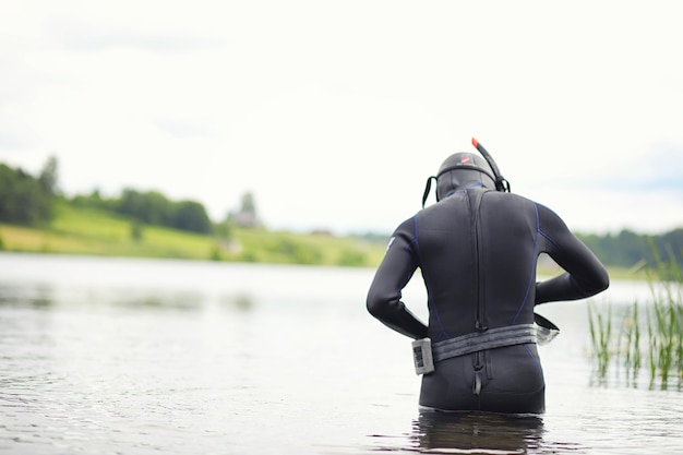 A scuba diver in a wet suit prepares to immerse in a pond