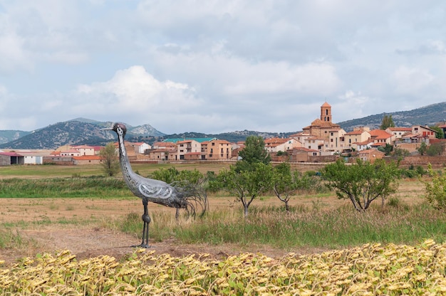 A sculpture of a crane in a field with the town of Gallocanta in the background