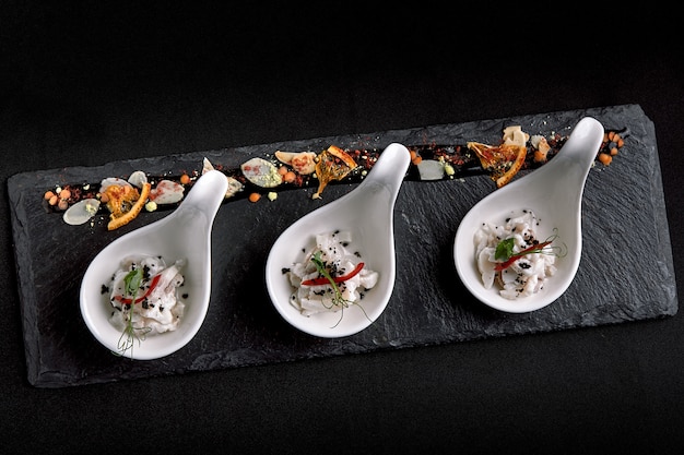 Sea bass ceviche mini portions served in beautiful Chinese spoons on a black plateau. Food concept for catering.