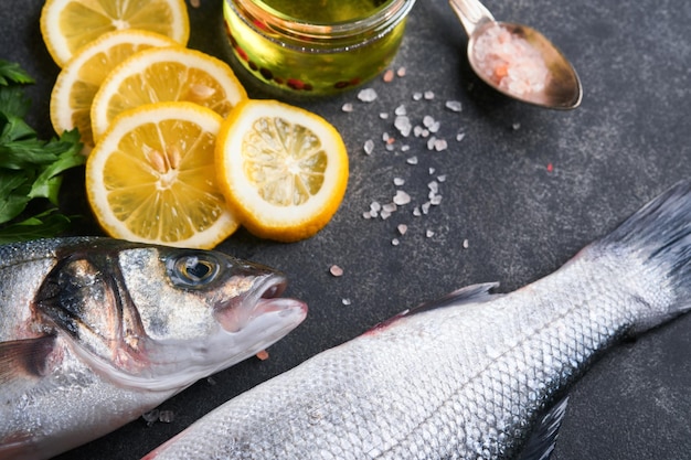 Sea Bass raw Fresh sea fish bass with salt pepper parsley olive oil and lemon on dark concrete rustic background Fresh fish ready to cook Food cooking background Top view copy space