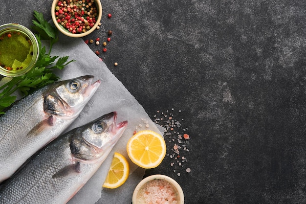 Sea Bass raw Fresh sea fish bass with salt pepper parsley olive oil and lemon on parchment paper on a dark concrete rustic background Food cooking background Top view copy space