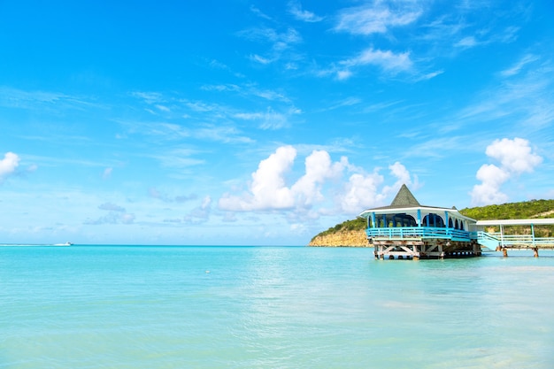 안티구아에서 화창한 날에 나무 쉼터가 있는 바다 해변. 푸른 하늘 배경에 청록색 물에 부두입니다. 카리브해의 여름 휴가. 방랑, 여행, 여행. 모험, 발견, 여행.