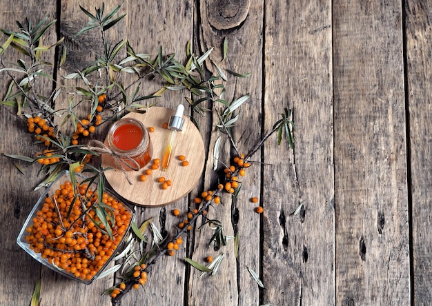 Sea buckthorn medicinal oil with sea buckthorn berries and branches on a wooden old background