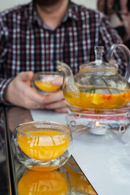 Sea buckthorn tea in a glass and teapot on the table