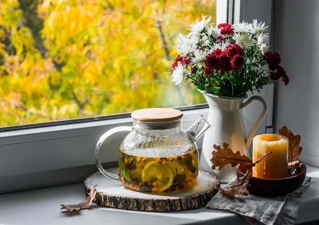 Sea buckthorn tea with herbs in a glass teapot on the window Cozy home autumn still life