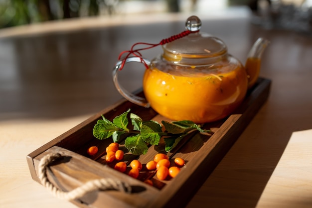 Sea buckthorn tea with mint in a transparent teapot on a wooden background in the rays of sunlight