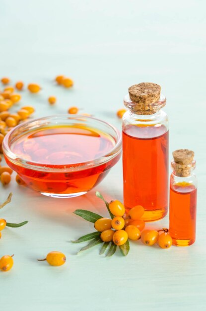 Sea buckthorn and two bottles bowl with sea buckthorn oil on blue table