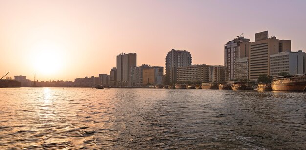 Sea by cityscape against sky during sunset