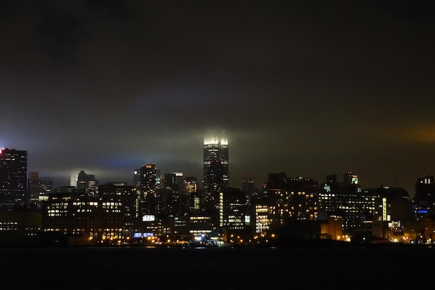 Sea by illuminated cityscape against sky at night