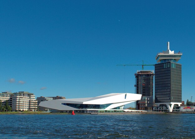 Sea by modern buildings against clear blue sky