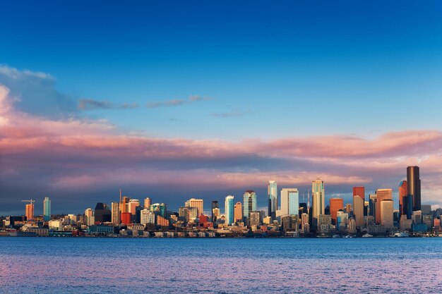 Sea by modern buildings against sky during sunset