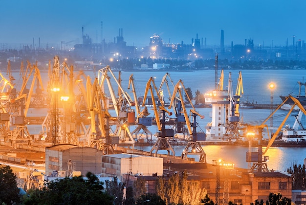 Sea commercial port and steel plant at night in Mariupol Ukraine before the war Industrial landscape Cargo freight ship with working cranes bridge in sea port at dusk Cargo port logistic