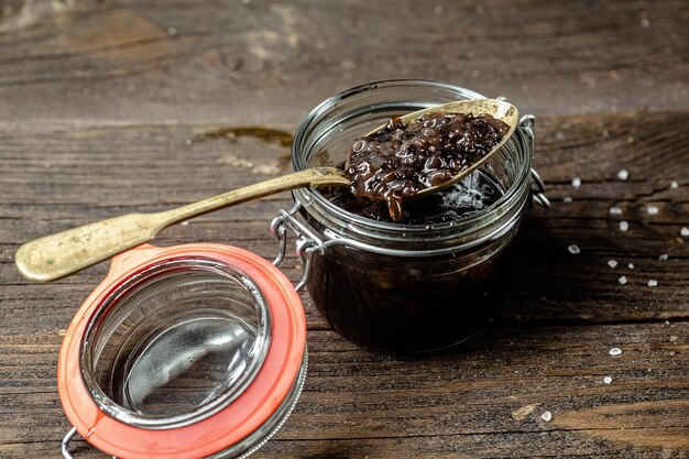 Photo sea cucumber or trepang, cut into small pieces, in a jar of glass, metal spoon, wooden cutting table