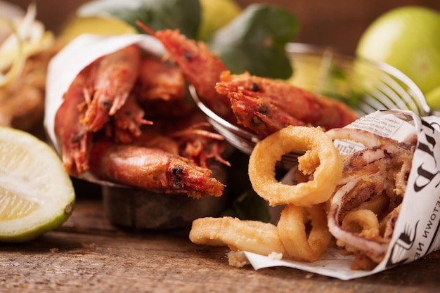 Sea food served on news paper: squid rings, grilled prawns, octopus, lemons on rustic wooden table. Close up