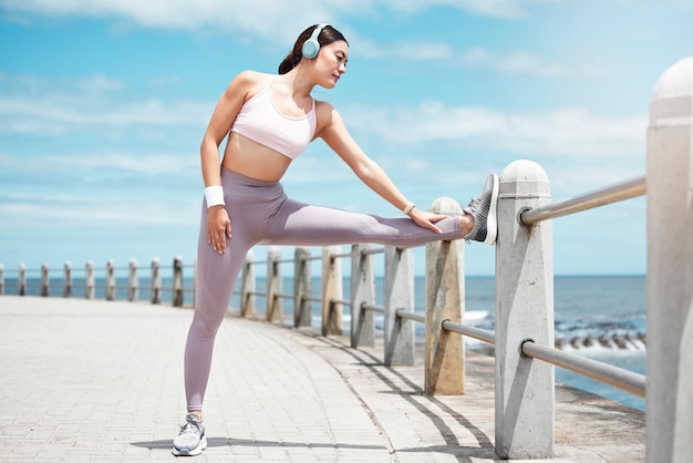 Sea headphone and woman stretching fitness or workout for wellbeing and health Wellness girl streaming audio music and training or exercise in nature at beach to relax healthy mind and body