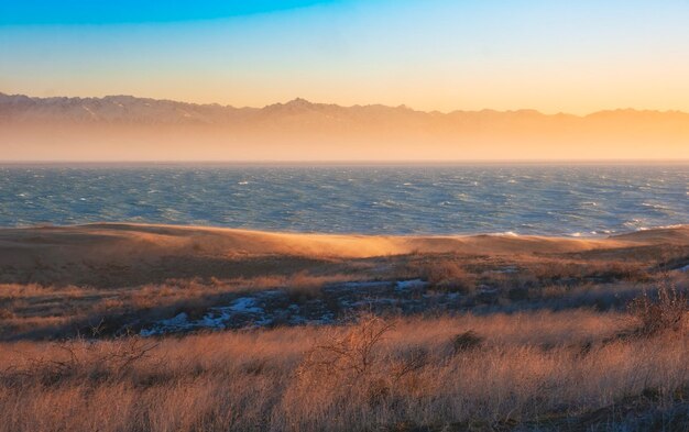 Foto il mare o il lago sullo sfondo di montagne innevate tra le dune durante il tramonto paesaggio