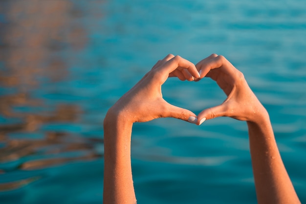 Foto mare amore. mani a forma di cuore in mare blu