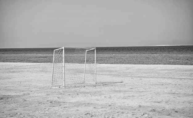 Sea or ocean shore coast with white soccer or football gate with net on golden sand ground sandy beach on bright sunny day on clear blue sky background Summer activity and sport