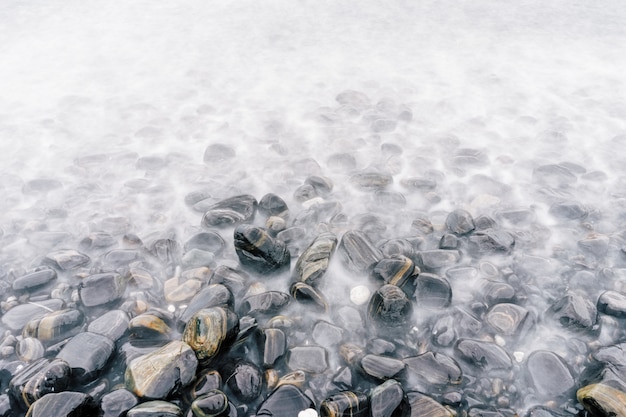 色とりどりの石、霧で透明な波と海の小石のビーチ